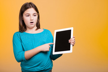 Amazed kid with a digital tablet in hands poiting at it on yellow background