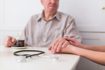 Close-up hands of older man and doctor who sitting at the table