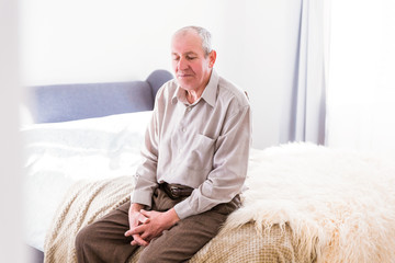 The old man sitting on a bed in the room at home