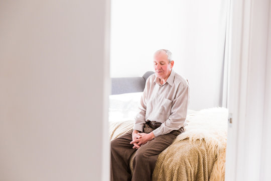 The Old Man Sitting On A Bed In The Room At Home And Looking Down