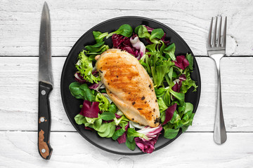 grilled chicken breast with mixed salad on a black plate with knife and fork