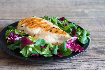 grilled chicken fillet with mixed salad on a black plate