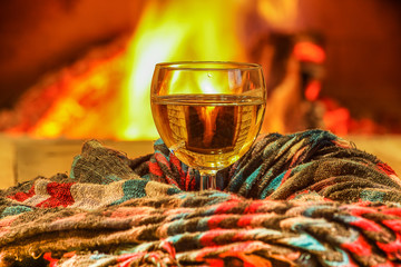 Glass of white wine against cozy fireplace background, winter vacation.