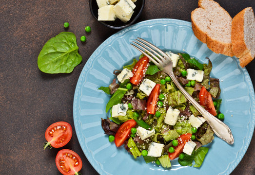 Vegetarian salad with blue cheese, tomatoes, green peas and sesame on a concrete background.