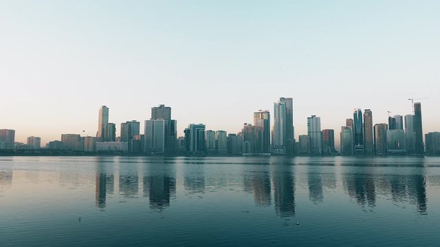 Panning along coast of Khalid lake. Skyline with skyscrapers. Al Noor island in Sharjah, UAE. Blue sky.