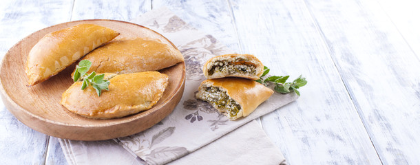 Fresh homemade pies with cheese and greens for breakfast. Portion pies. On a wooden plate and on a white background. Free space for text or advertising.