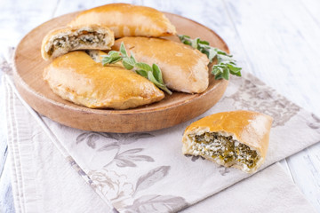 Fresh homemade pies with cheese and greens for breakfast. Portion pies. On a wooden plate and on a white background. Free space for text or advertising.