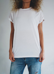 An attractive young woman dressed in a white blank t-shirt and blue jeans posing on a background of a white wall. Vertical mock up. empty space for you logo or design