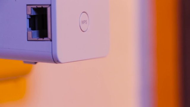 Man insert WiFi repeater into electrical socket on the wall and press with his finger on WPS button