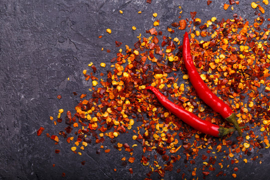 Chili peppers and flakes on black stone background, fresh and seeds. Copy space