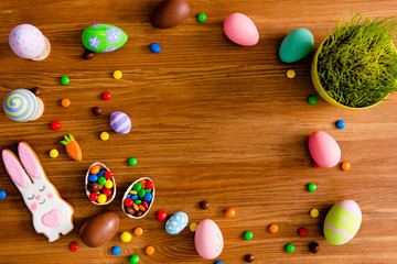 Top view portrait with copy space for text of easter objects, on wooden brown background laying painted eggs, flower, baked cookies in carrot and hare figure