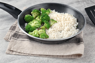 Frying pan with rice and broccoli on table