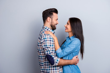 Portrait of caucasian, attractive, smiling couple - bearded man embrace his charming, cute, pretty woman, looking to each other while standing over grey background