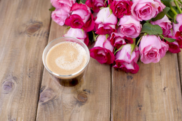 Obraz na płótnie Canvas A bouquet of fresh pink roses and a glass of espresso. Wooden background. Free space for text or postcards. 