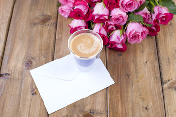 A bouquet of fresh pink roses and a glass of espresso. Wooden background. Free space for text or postcards. White envelope for writing.