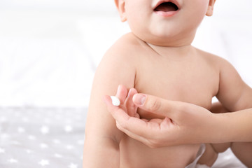 Woman applying body cream on her baby against light background © Africa Studio