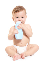 Cute baby with bottle of body cream on white background