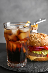 Glass of cold cola with tasty burger on slate plate