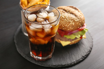 Glass of cold cola with tasty burger on slate plate