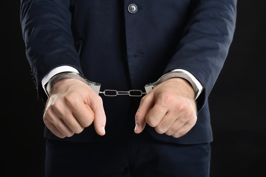 Businessman in handcuffs on black background