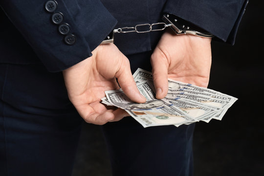Businessman in handcuffs holding bribe on black background, closeup