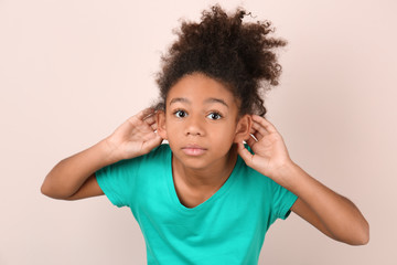 Little African-American girl with hearing problem on light background