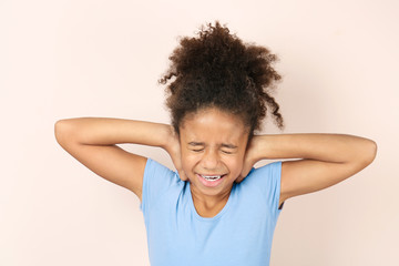 Little African-American girl covering her ears on light background. Hearing problem