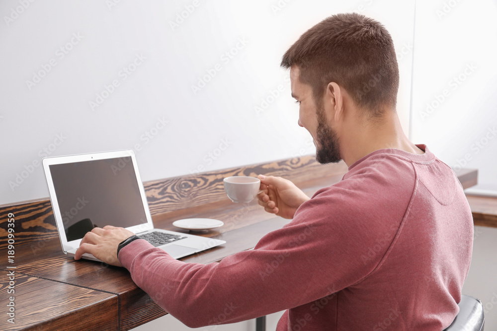 Sticker Young man using modern laptop in cafe