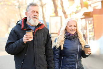 Happy mature couple walking in the street and drinking coffee on autumn day