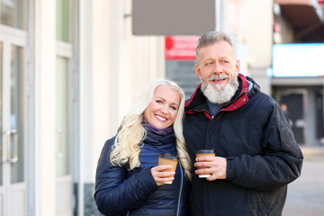 Happy mature couple walking in the street and drinking coffee on autumn day