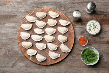 Wooden board with raw dumplings on table, top view