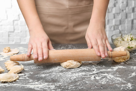 Woman rolling dough on table, closeup. Cooking dumplings