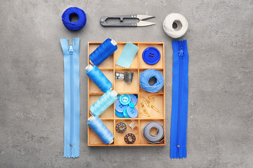 Colorful threads and sewing accessories on grey background