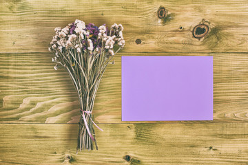Beautiful bouquet of flowers and empty paper for text on wooden table.