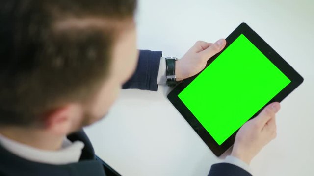 A man using an iPad with a green screen indoors. View from the top. Close-up shot. Soft focus.