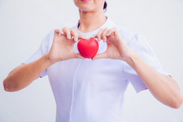 A nurse holding red heart toy. She is Left / right hand holding it. She is smile and good mood. The photo shows the principle of caring and good health.