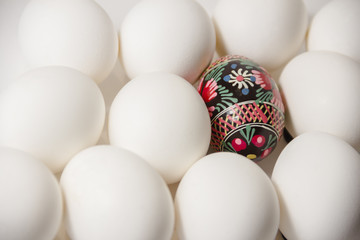 Handmade folk culture decorated easter egg laying among white plain eggs. easter coming soon.