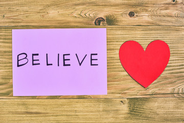 Paper with word believe and heart shape on wooden table,believe in love concept.