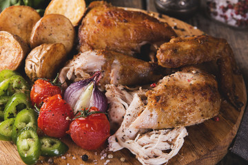 baked, fried chicken with tomatoes, pepper, potatoes on the board