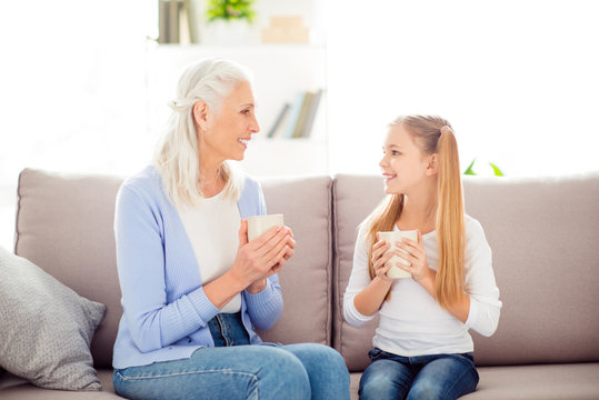 Grandparent adopted child comfort  international women's day concept. Two joyful excited delightful lovely cute sweet schoolgirl and adult calm peaceful granny gossiping talking in livingroom