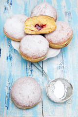 Tradycyjne polskie pączki z cukrem pudrem i dżemem na niebieskim drewnianym tle, podawane w tłusty Czwartek. 