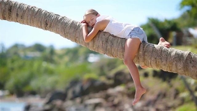 Little girl at tropical beach sitting on palm tree during summer vacation