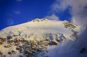 High icy mountain peak with glacier and blue sky on sunset