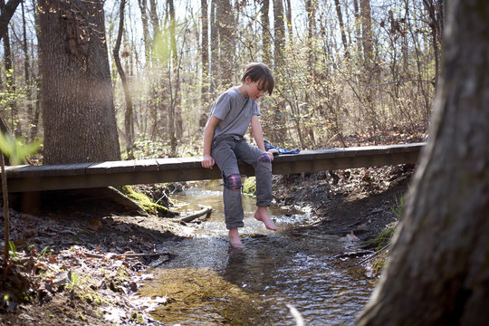 Boy Sitting on Bridge Over Creek