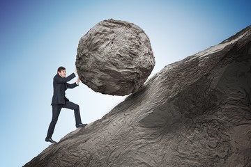 Sisyphus metaphore. Young businessman pushing heavy stone boulder up on hill. © vchalup