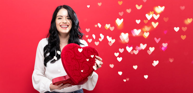 Happy young woman holding a big heart gift box with heart lighs