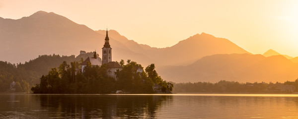Fototapeta na wymiar Island in lake Bled with orange Julian Alps sillhouette