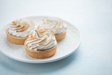 Delicious lemon tartlets with meringue on a white vintage plate. Sweet treat on a light blue background