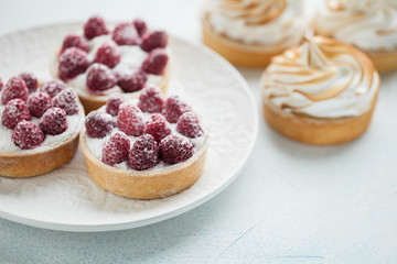 Delicious lemon and raspberry tartlets with meringue on a white vintage plate. Sweet treat on a light blue background