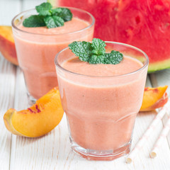 Watermelon, peach, mint and coconut milk smoothie in a glass on white wooden background, square format